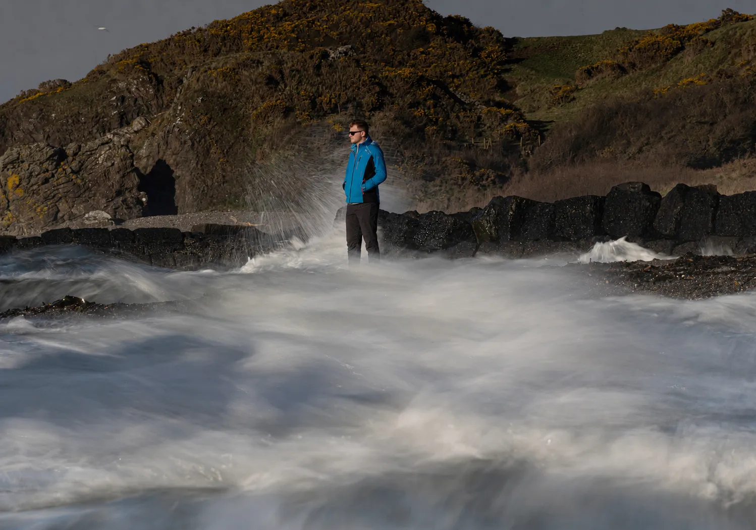 Luke McIlwaine on the Northern Ireland coast as waves break over the rocks